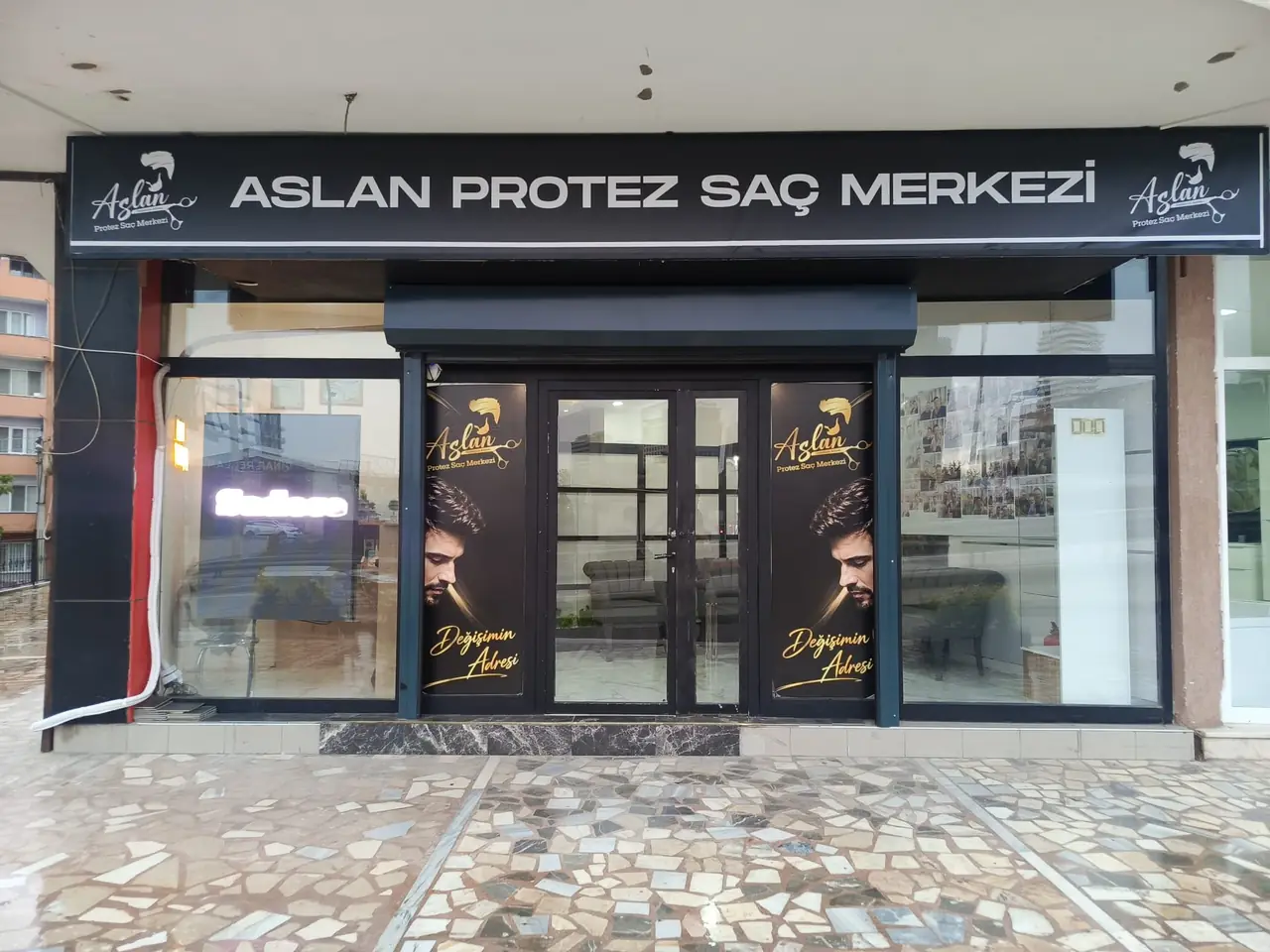 Siyah tabelasında Aslan Protez Saç Merkezi yazan, cam cepheli merkez girişi